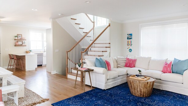 A modern living room with a staircase, white furniture, and a blue rug.
