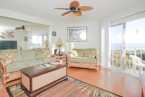 Relax in this spacious living room with a high ceiling, ceiling fan, and large window offering a view of the outdoors. Enjoy the sofas, coffee table, TV, and lamp.