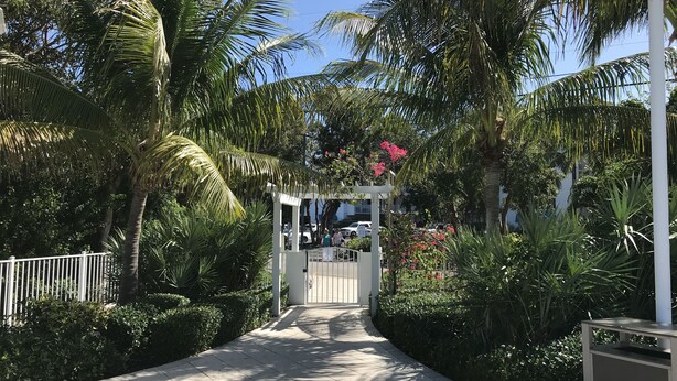 A pathway leading to a gated entrance surrounded by lush greenery and palm trees. - Keys Deal w/Cafe & Pool Bar! Up to 20% Off Oceanfront 2/2 with Private Beach (Tavernier)