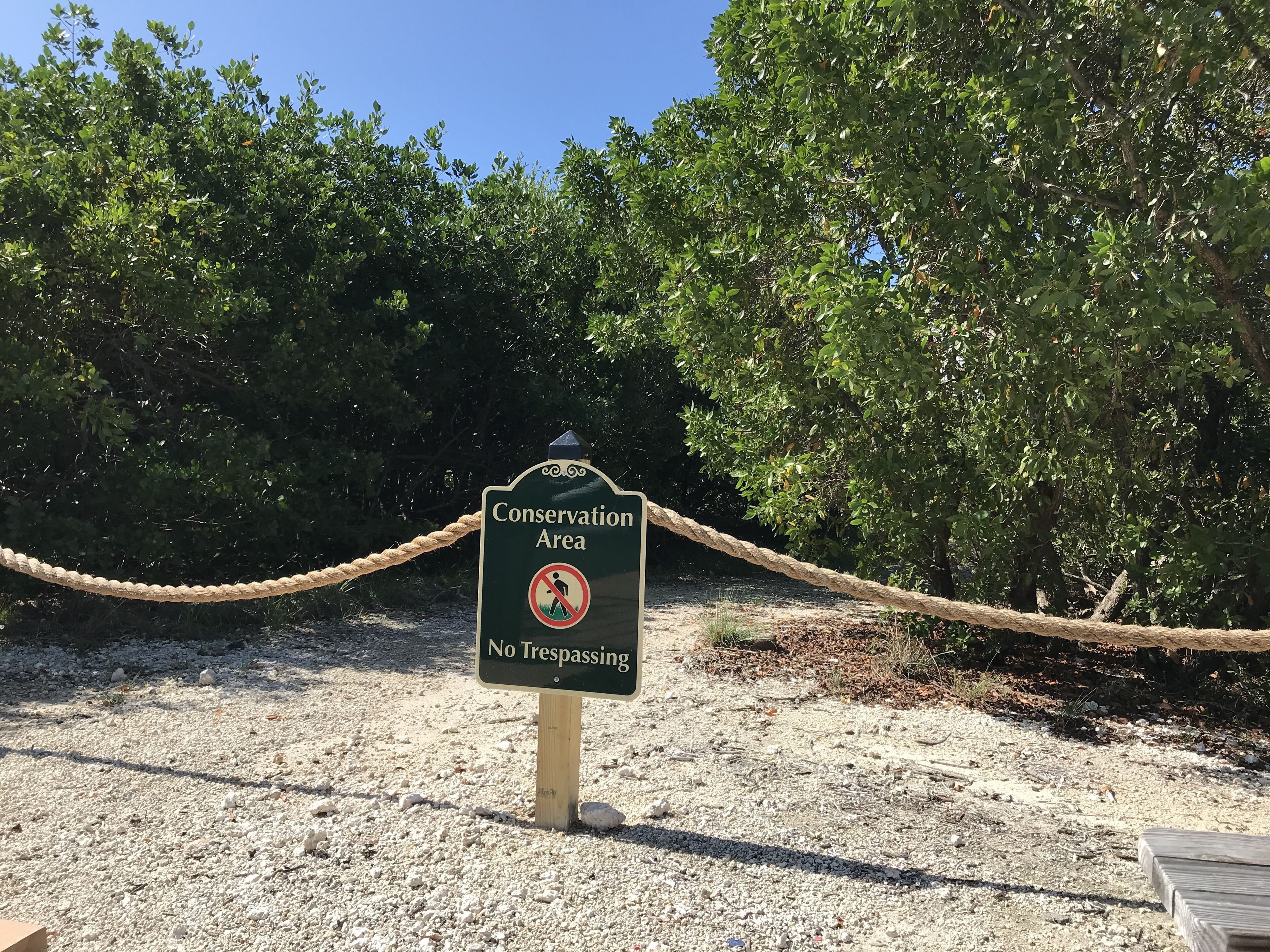 A sign indicating a conservation area with a rope barrier and a no trespassing symbol.