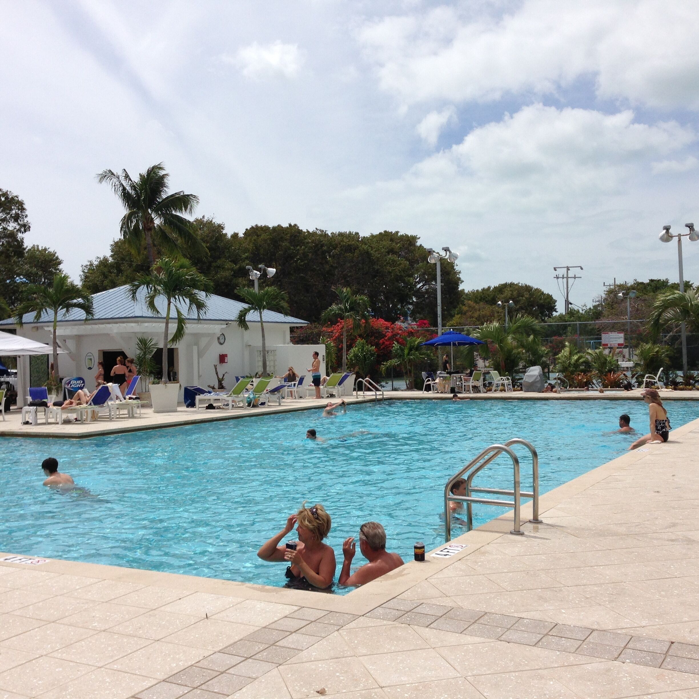 A swimming pool with people swimming and relaxing. There are lounge chairs and umbrellas around the pool.
