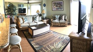 A living room with a sofa, chairs, a coffee table, a TV, and a dining area with stools. - Keys Deal w/Cafe & Pool Bar! Up to 20% Off Oceanfront 2/2 with Private Beach (Tavernier)