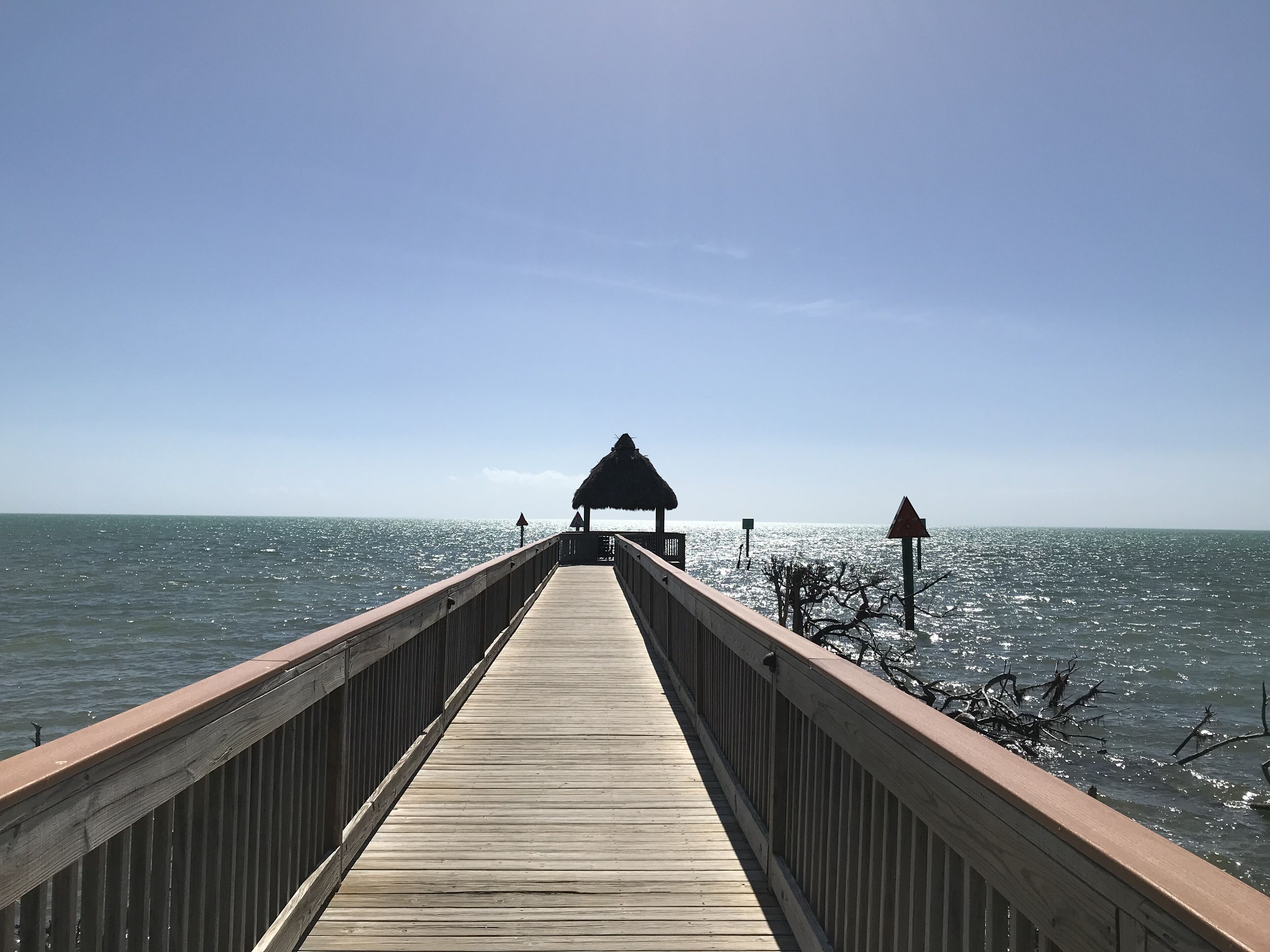A wooden pier extending into the sea with a thatched-roof structure at the end.