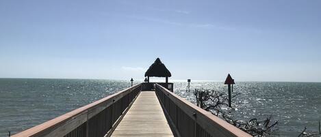 A wooden pier extending into the sea with a thatched-roof structure at the end.