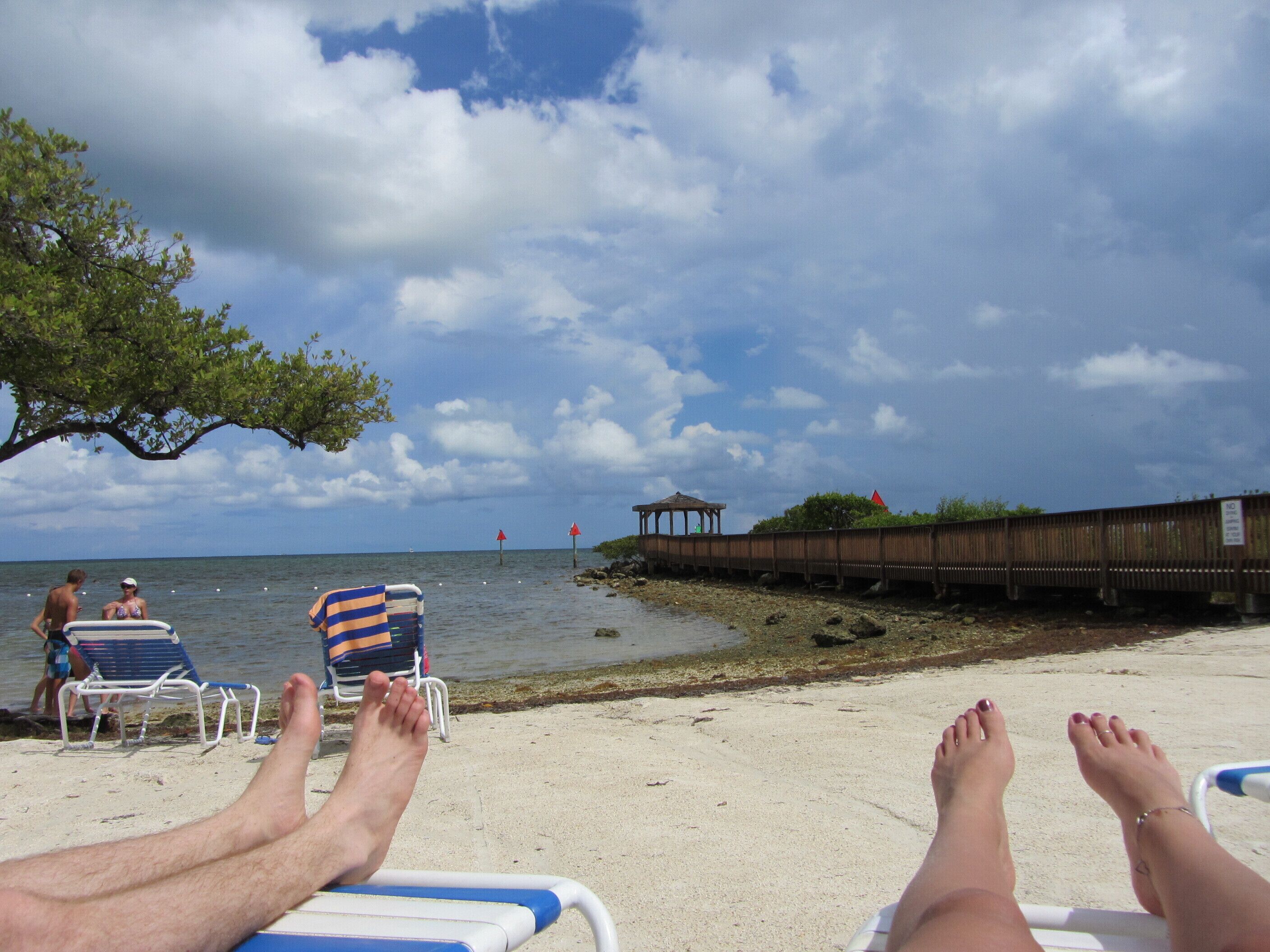 A beach scene with lounge chairs, a wooden structure, and a clear sky.
