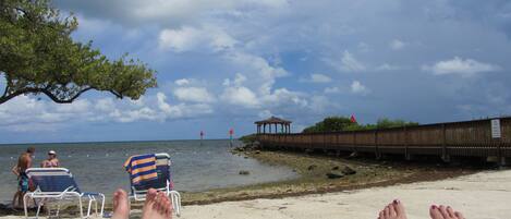 A beach scene with lounge chairs, a wooden structure, and a clear sky.