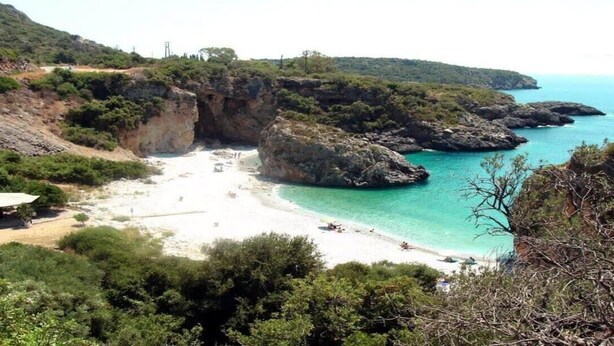 A coastal landscape with a sandy beach, rocky cliffs, and a clear blue sea.