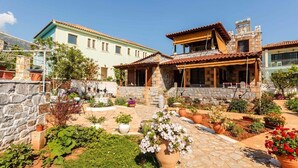 A courtyard with stone walls, potted plants, and a two-story building with a tiled roof.
