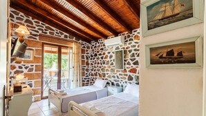A room with two beds, a stone wall, wooden beams, a balcony, and a framed picture of a ship.