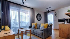 A modern living room with a grey sofa, wooden coffee table, and a large window with curtains. - Antałówka 12 Apartamenty wysoki standard (Zakopane)