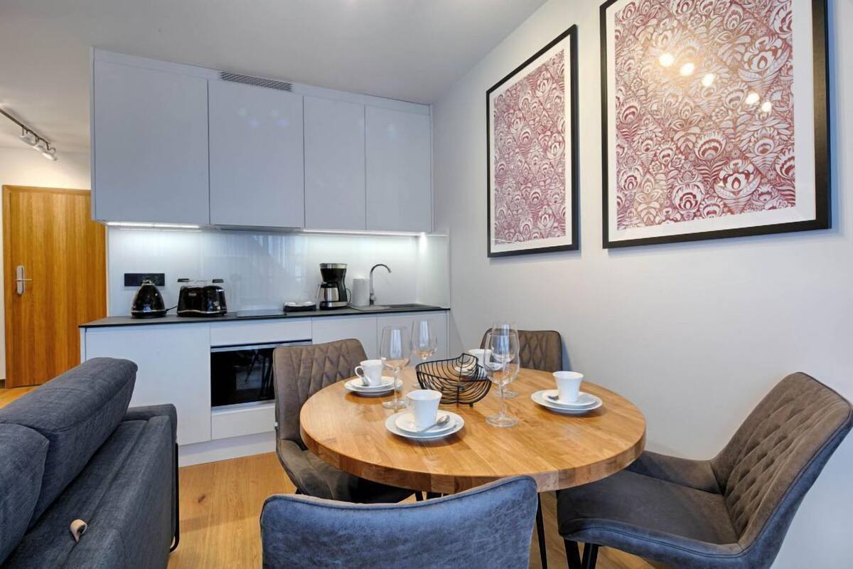 A modern kitchen with white cabinets, a dining table set with plates, cups, and glasses, and two framed artworks on the wall.
