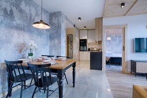 Une cuisine moderne avec des meubles en bois, un coin repas avec une table en bois et des chaises noires, et un téléviseur fixé au mur.