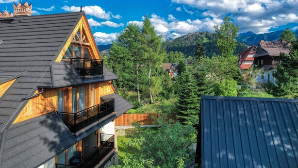 A multi-story wooden house with a balcony, surrounded by lush greenery and mountains in the background. - Antałówka 12 Apartamenty wysoki standard (Zakopane)