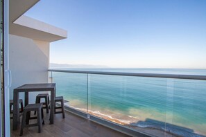 A balcony with a table and chairs overlooking a beach and the ocean.