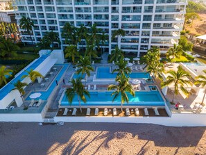 Un hotel con amplias zonas de piscina, palmeras y una playa.