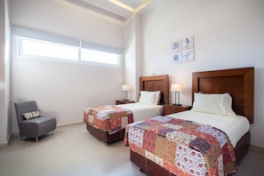 Habitación de hotel con dos camas, una silla y un ventanal.