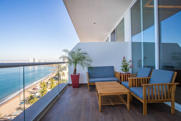 Un balcón con vista a la playa y el océano, muebles de madera y una planta en maceta.