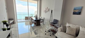 En moderne stue med en glasgulv, der fører til en balkon, et spiseområde og et arbejdsområde med en bærbar computer.