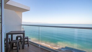 A balcony with a table and chairs overlooking a beach and the sea.