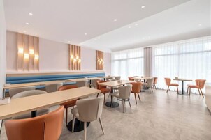 Un comedor moderno con asientos tipo banca y mesas, ventanas amplias y un suelo de tonos claros.