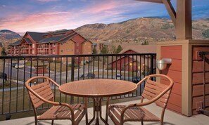 A balcony with wicker furniture, a view of a mountainous landscape, and a building with red and brown exteriors.
