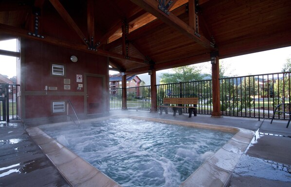A hot tub area with a wooden roof, a bench, and a fenced patio.