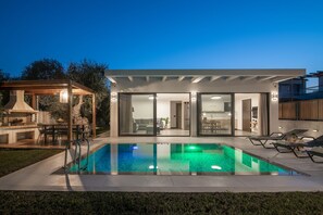 Ein modernes Haus mit Schwimmbad, Sitzgelegenheiten im Freien und einer Terrassenfläche.