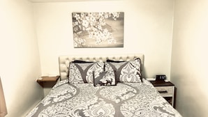 A bedroom with a tufted headboard, a patterned bedspread, and a nightstand with a clock.