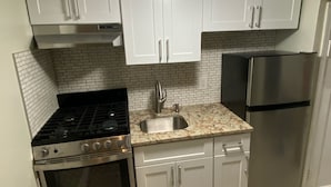 A compact kitchen with white cabinets, a stainless steel stove, a sink, and a refrigerator.