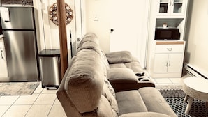 A living room with a sofa, a clock, a microwave, and a refrigerator.