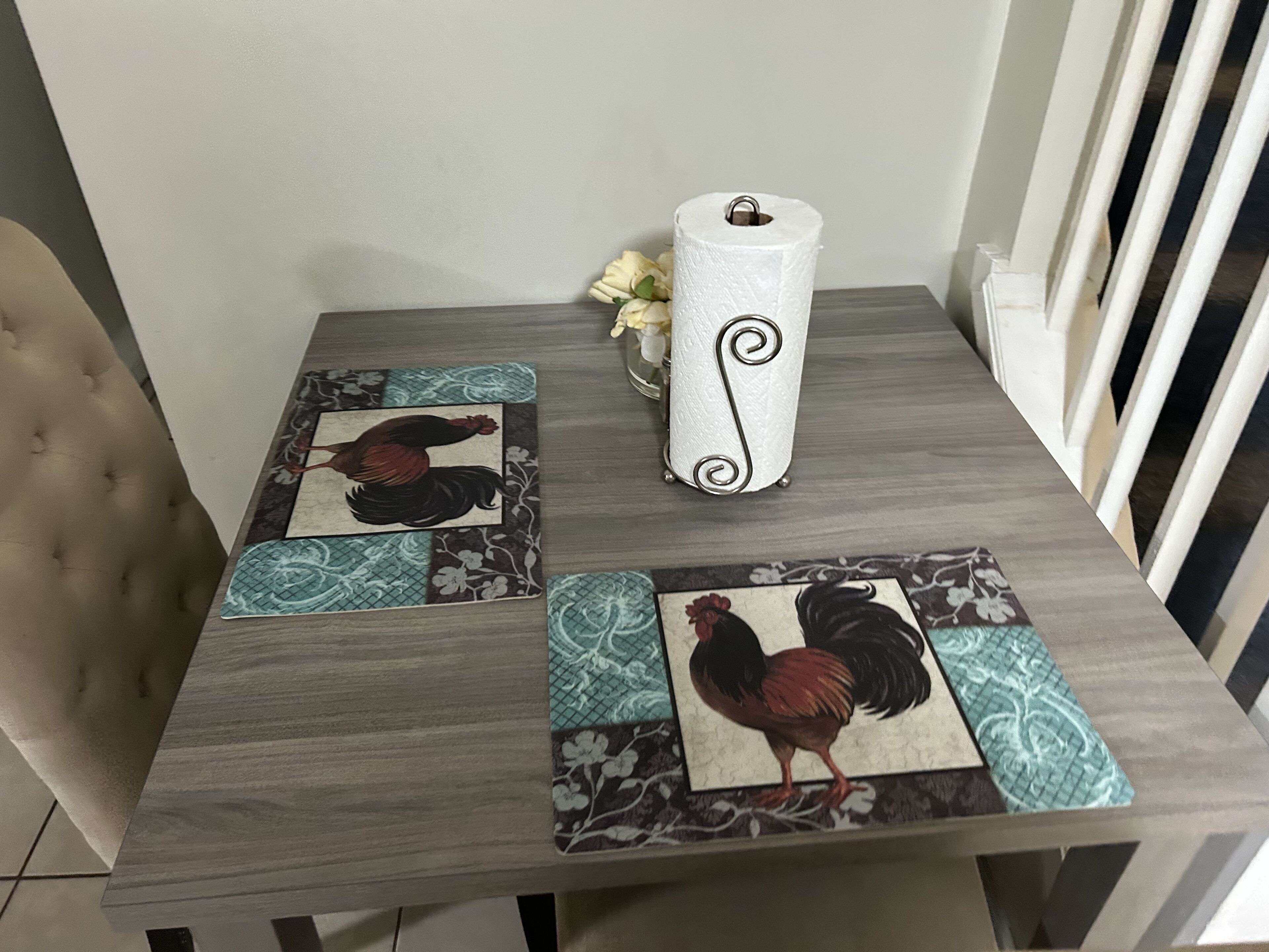 Ein Esstisch mit gemustertem Tischläufer, einer dekorativen Vase mit Blumen und einer Toilettenpapierrolle.