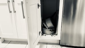A kitchen with white cabinets, a stainless steel refrigerator, and a pot inside a cabinet.