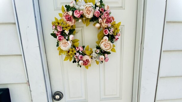 A white door with a wreath of pink and white flowers.