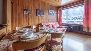 A dining area with wooden walls, a table set for four, and a view of a snowy landscape through a window.
