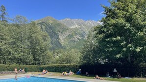 A swimming pool with people relaxing and swimming, surrounded by lush greenery and mountains in the background.
