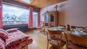 A cozy room with a wooden ceiling, a dining table set with plates and glasses, a cabinet, and a chair.