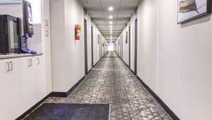 A long, narrow hallway with patterned carpet, white walls, and a fire extinguisher mounted on the wall.
