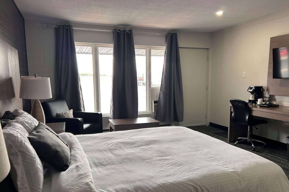 Quarto de hotel com uma cama grande, uma escrivaninha com cadeira, televisão e janela com cortinas.