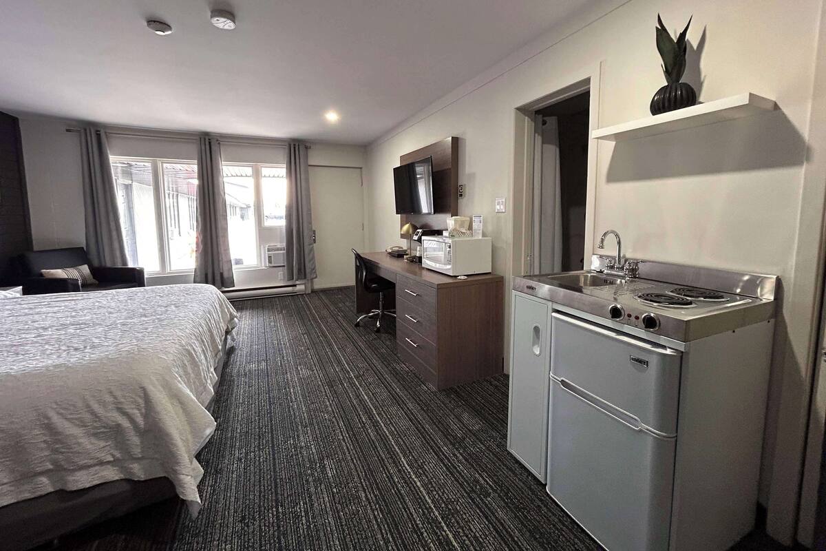 Quarto de hotel com cama, escrivaninha, cozinha compacta e banheiro.