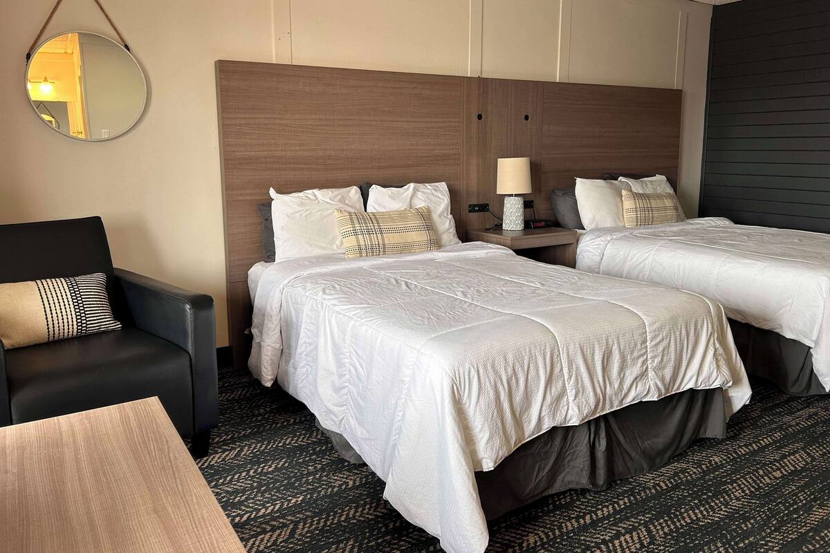 Quarto de hotel com duas camas, uma escrivaninha, uma cadeira e um espelho pendurado.