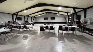 A large indoor space with high ceilings, multiple tables and chairs arranged for meetings, and a flat-screen TV mounted on the wall.