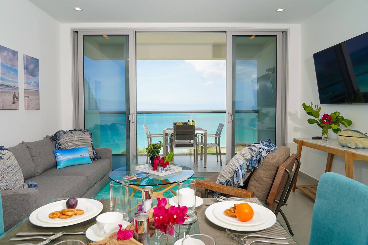 Un salón moderno con balcón vistas al mar, amoblado con sofá, mesa de comedor y sillas.
