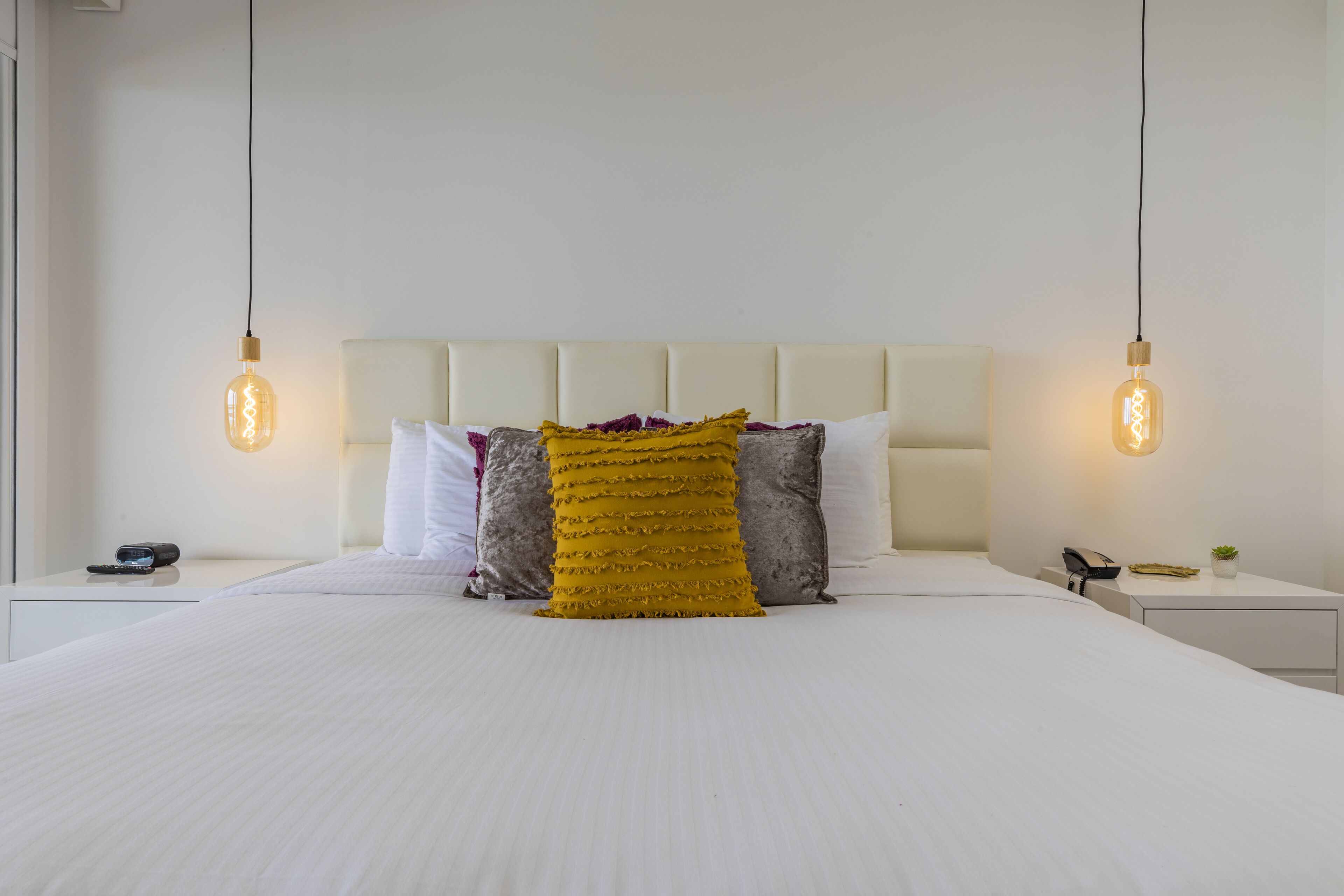 A neatly made bed with a white headboard, two bedside tables, and a nightstand with a lamp.