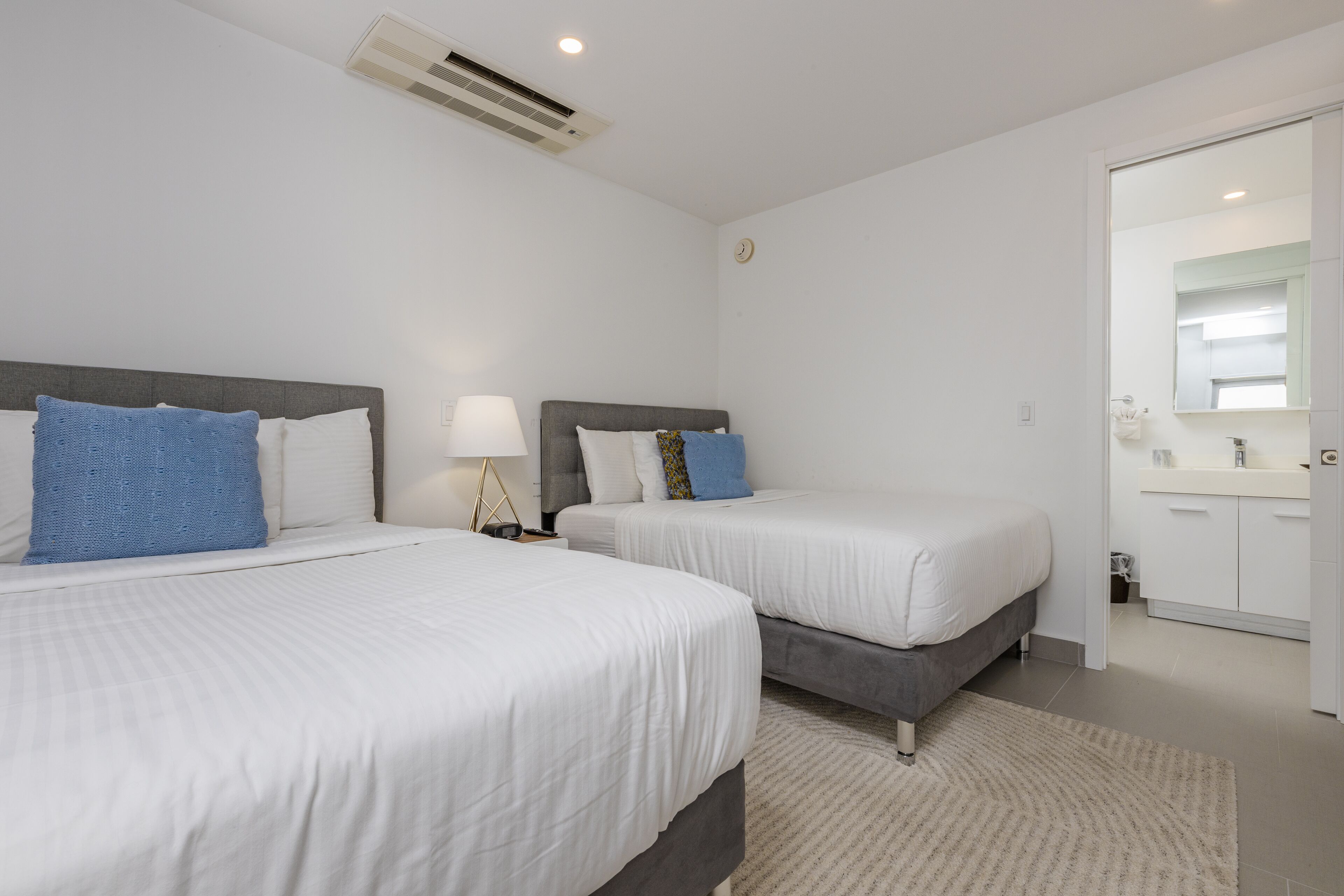 A hotel room with two beds, a bathroom with a mirror, and a door leading to another room.