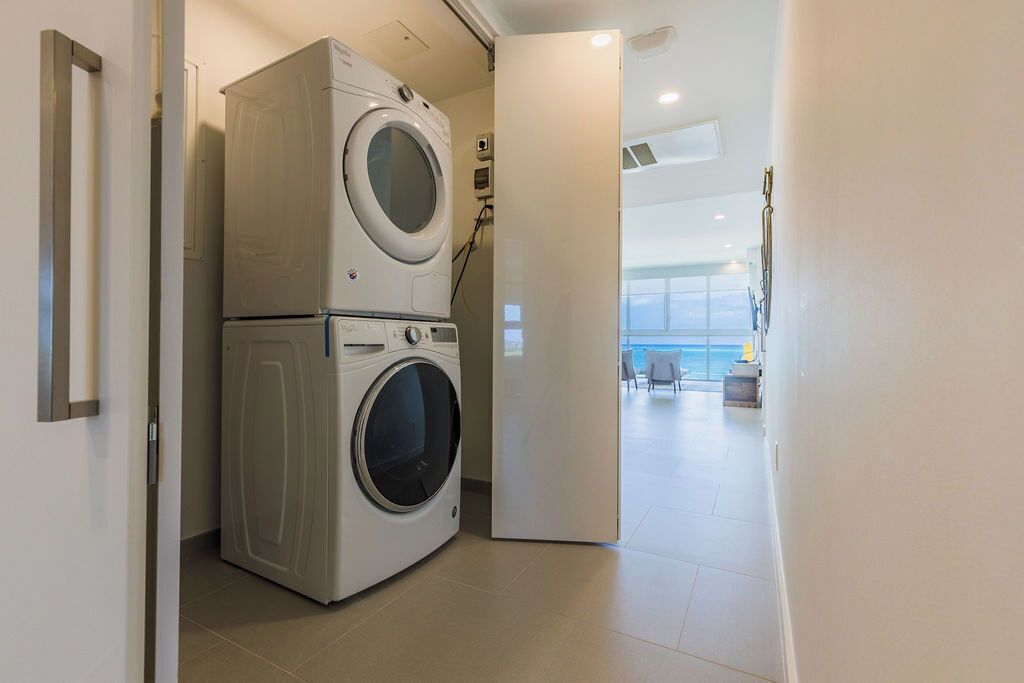 Une buanderie équipée de machines à laver et de sèche-linge superposés, une vue sur l’océan par une grande fenêtre et un aménagement intérieur moderne.