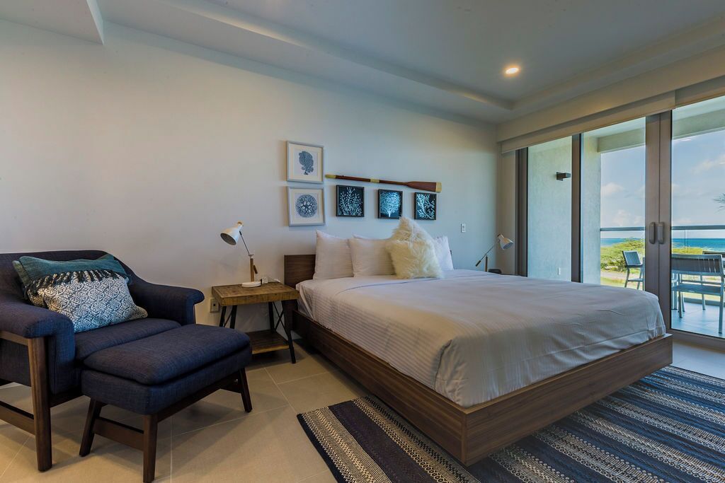 Une chambre dotée d’un grand lit, d’une chaise, d’une table de chevet et offrant une vue sur l’extérieur grâce à une porte coulissante.