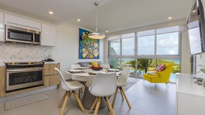 A modern kitchen with a dining area, large windows, and a view of the outdoors. - Azure Beach Residences (Noord)