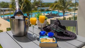 A balcony with a bottle of champagne, two glasses of orange juice, a book, and sunglasses on a table. - Azure Beach Residences (Noord)