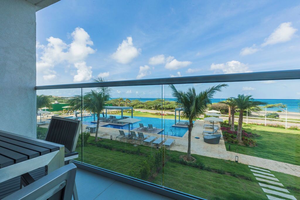 Un balcon avec vue sur une piscine, des chaises longues et des palmiers.