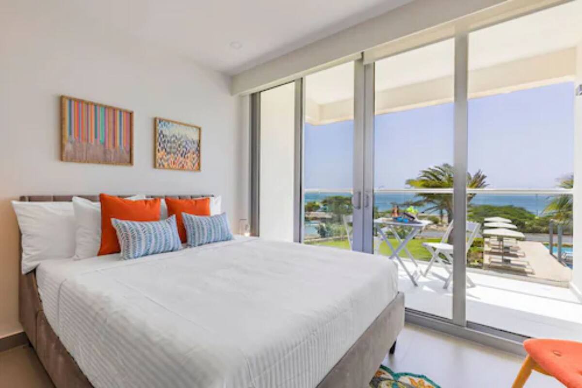 Un dormitorio con una cama grande, vista al océano y un balcón con mobiliario exterior.